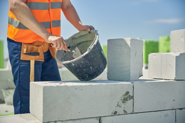 Cropped photo of a bricklayer scooping the mortar with a trowel from a metal bucket