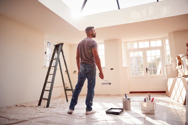 Rear View Of Man Holding Paint Roller Decorating New Home